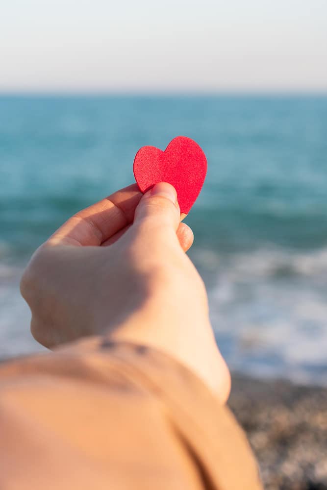 Hand hält rotes Herz am Meer als Symbol für die Verbundenheit bei einer Seebestattung