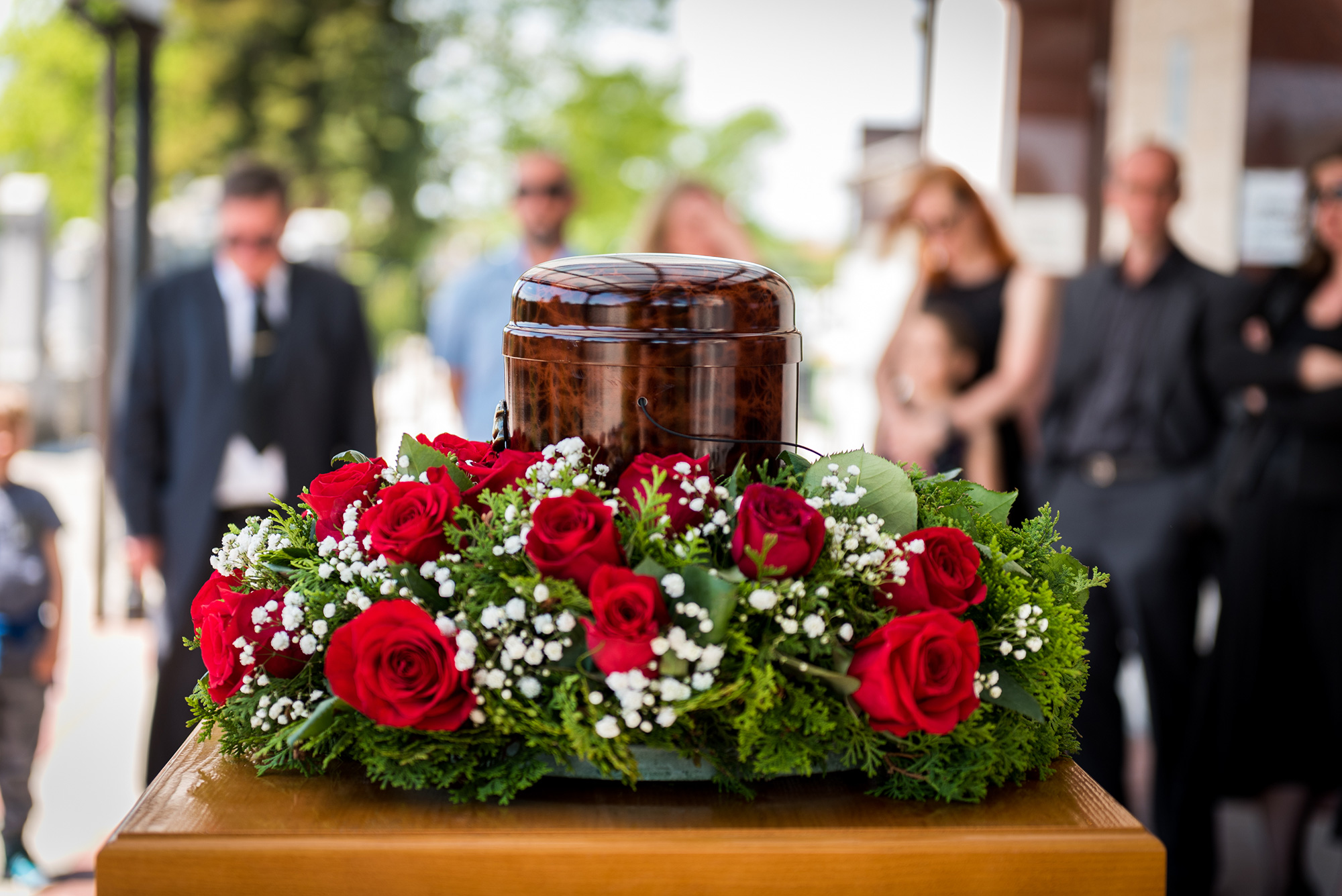 Urne mit Blumenschmuck bei einer Feuerbestattung, Angehörige im Hintergrund
